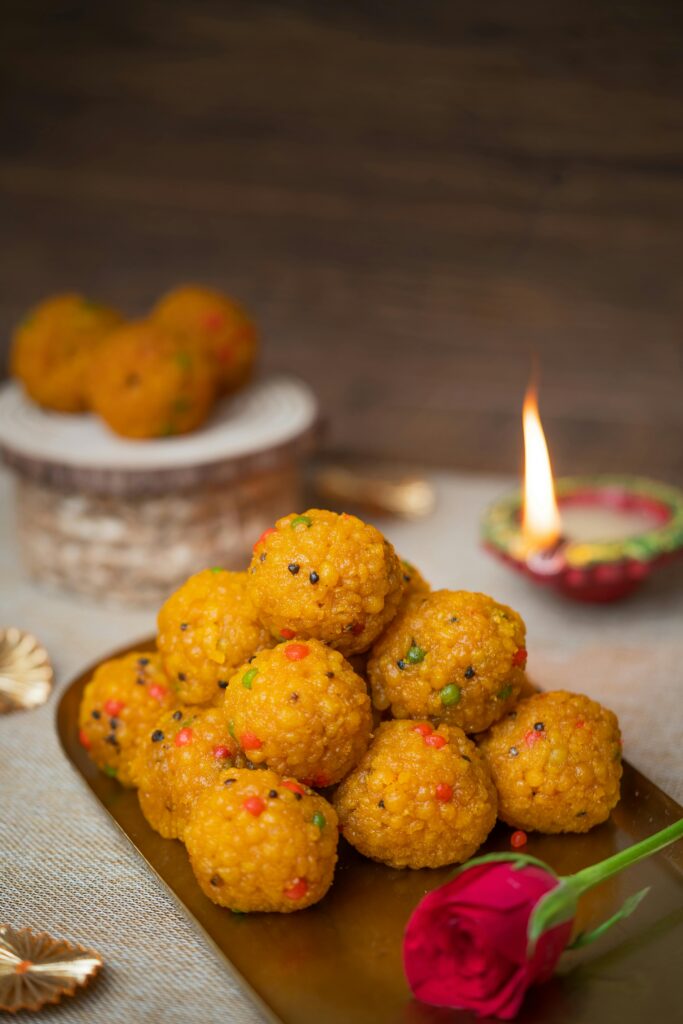 Delicious Indian sweets on a brass plate, accompanied by a festive diya and red rose, perfect for celebrations.